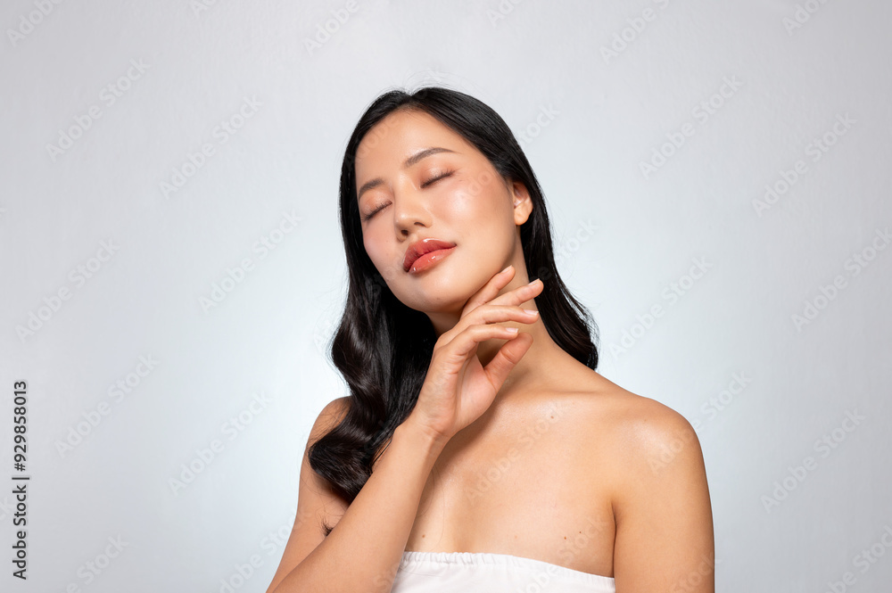 A young Asian beauty poses against a grey background, gently touching her face with her eyes closed. A young Asian beauty poses against a grey background, gently touching her face with her eyes closed.