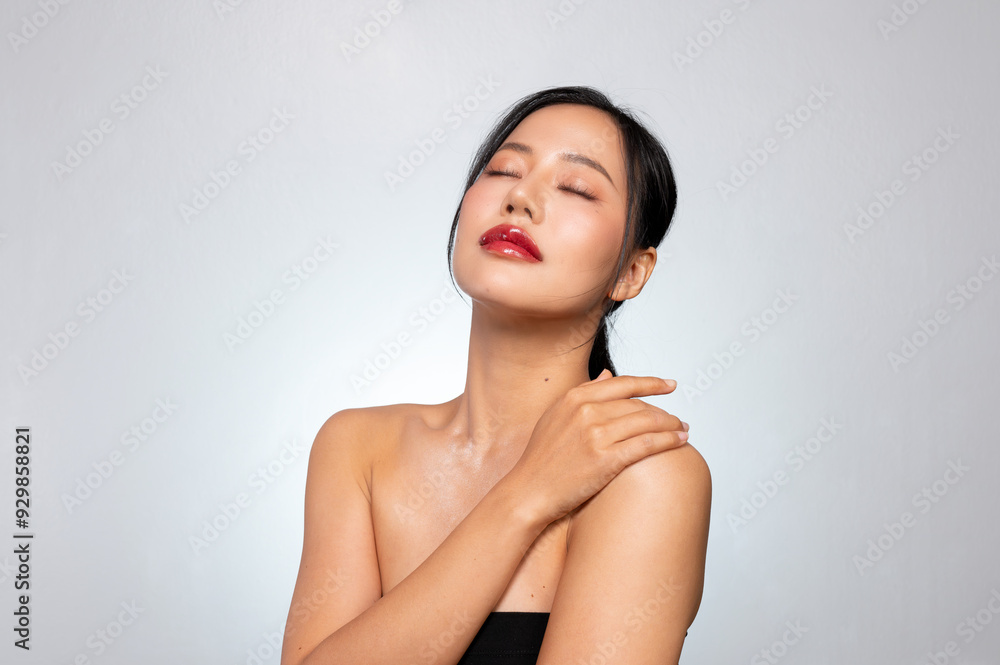 A gorgeous Asian beauty model with glowing tanned skin poses, touching her skin with her eyes closed A gorgeous Asian beauty model with glowing tanned skin poses, touching her skin with her eyes closed