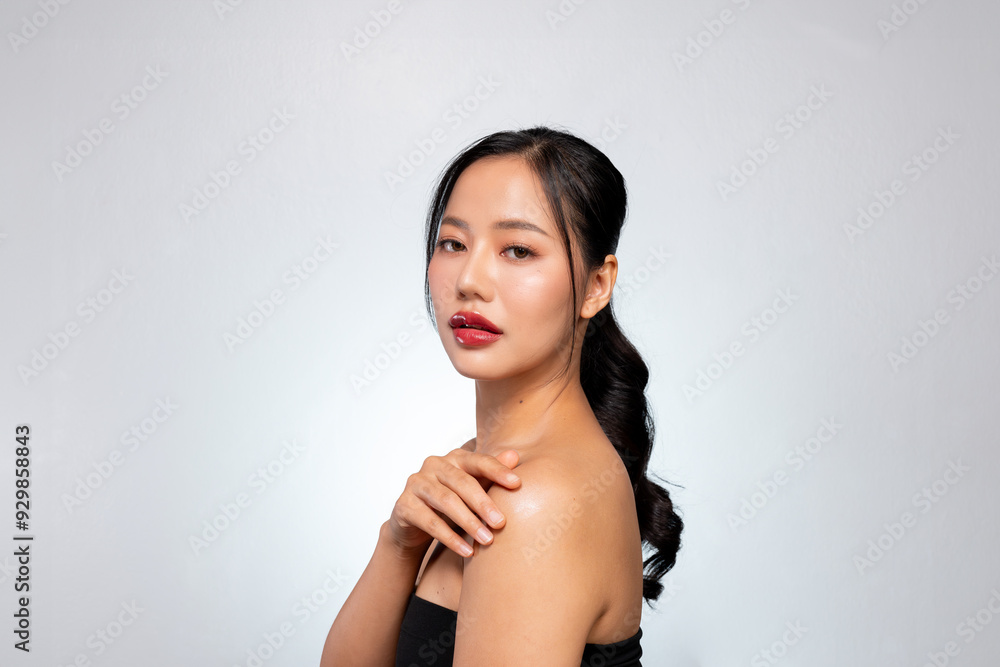 A gorgeous Asian model touches her glowing tanned skin while posing against a grey studio background A gorgeous Asian model touches her glowing tanned skin while posing against a grey studio background