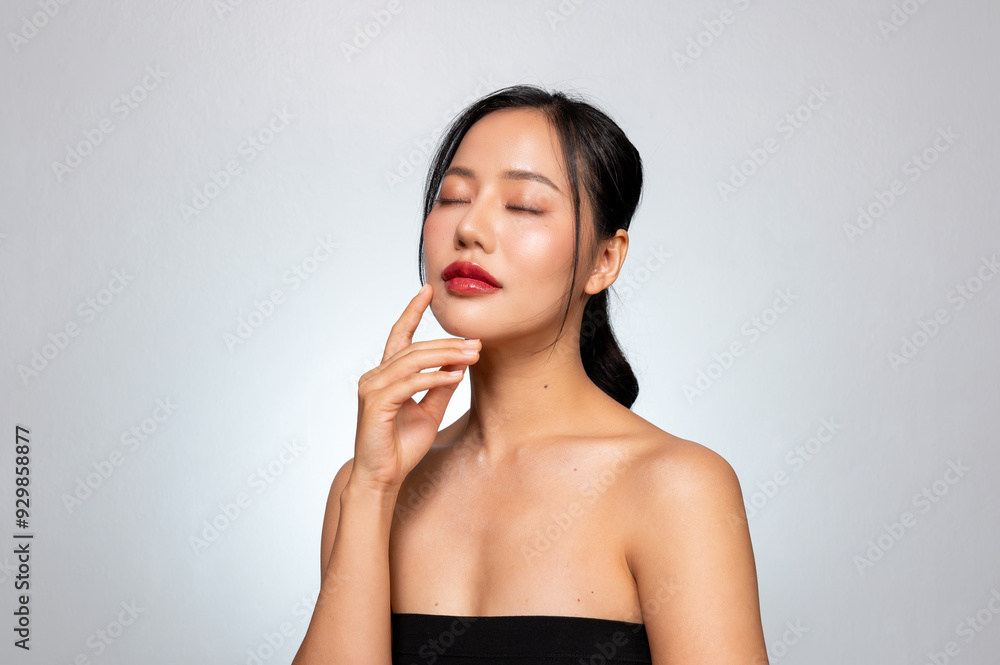 A young Asian woman with a perfect, beautiful face, touching her face with her eyes closed. A young Asian woman with a perfect, beautiful face, touching her face with her eyes closed.