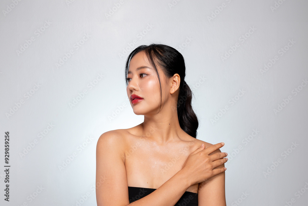 A gorgeous Asian woman touches her glowing, healthy tanned skin, posing against a grey background. A gorgeous Asian woman touches her glowing, healthy tanned skin, posing against a grey background.