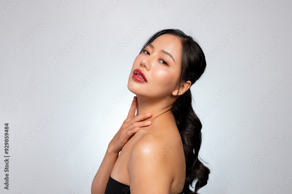 Gorgeous Asian woman with tanned skin and beautiful makeup touches her neck and looks at the camera. Gorgeous Asian woman with tanned skin and beautiful makeup touches her neck and looks at the camera.