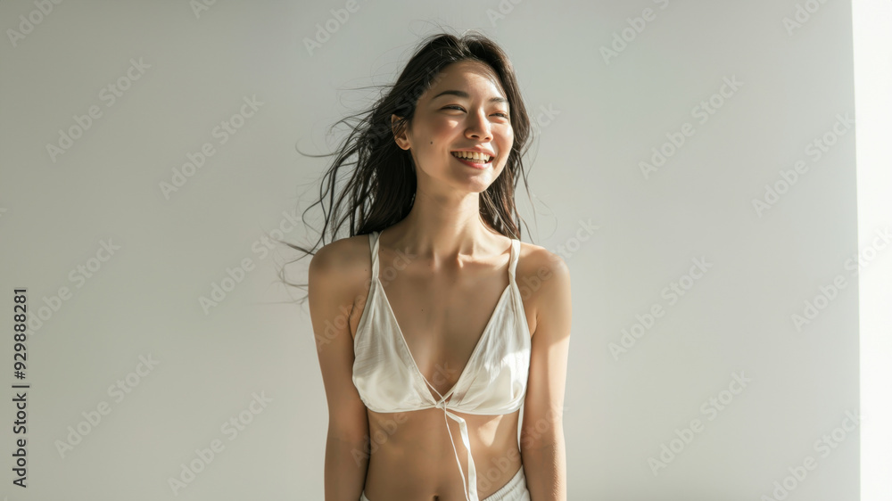 Fototapeta premium A young woman with a radiant smile poses confidently in a white bikini top. Her carefree expression and flowing hair exude a sense of joy and freedom.