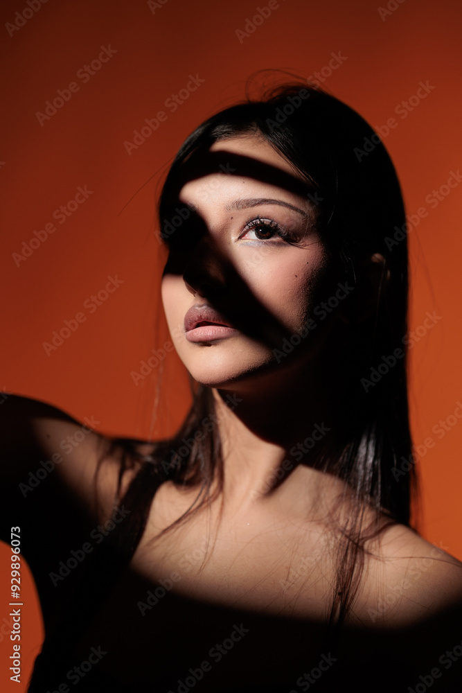 Fototapeta premium Brunette girl posing in a beam of light in the studio, on a red background, light and darkness.