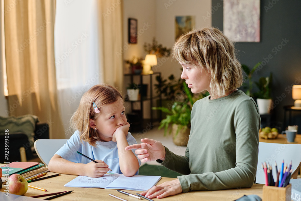 Mother explaining grammar rules to her little girl while they doing homework Mother explaining grammar rules to her little girl while they doing homework