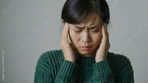 Beautiful stressed Asian woman in green sweater touching