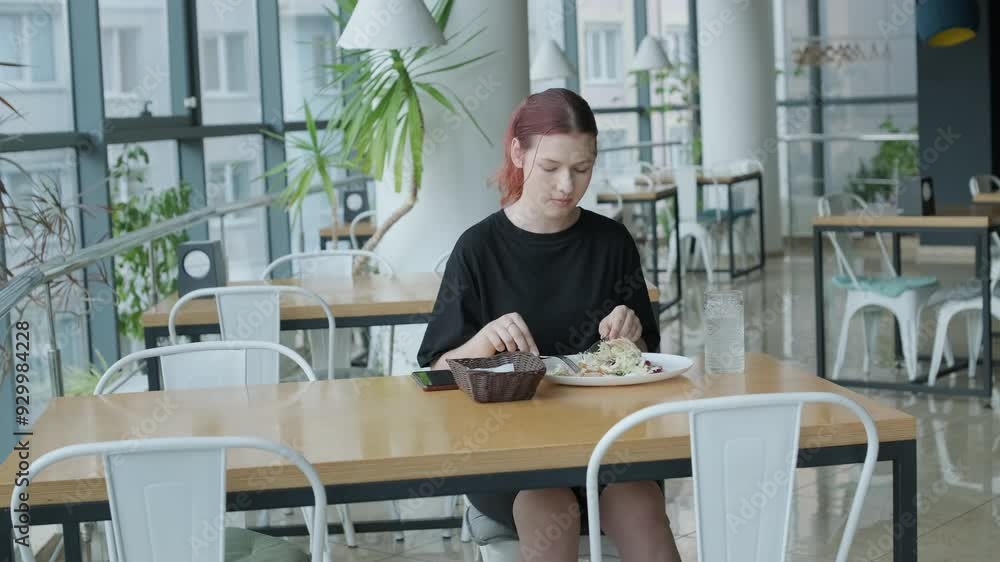 Young woman eating a fresh salad at a wooden table in a modern restaurant with large windows, natural light, and urban views. Relaxed dining scene Young woman eating a fresh salad at a wooden table in a modern restaurant with large windows, natural light, and urban views. Relaxed dining scene