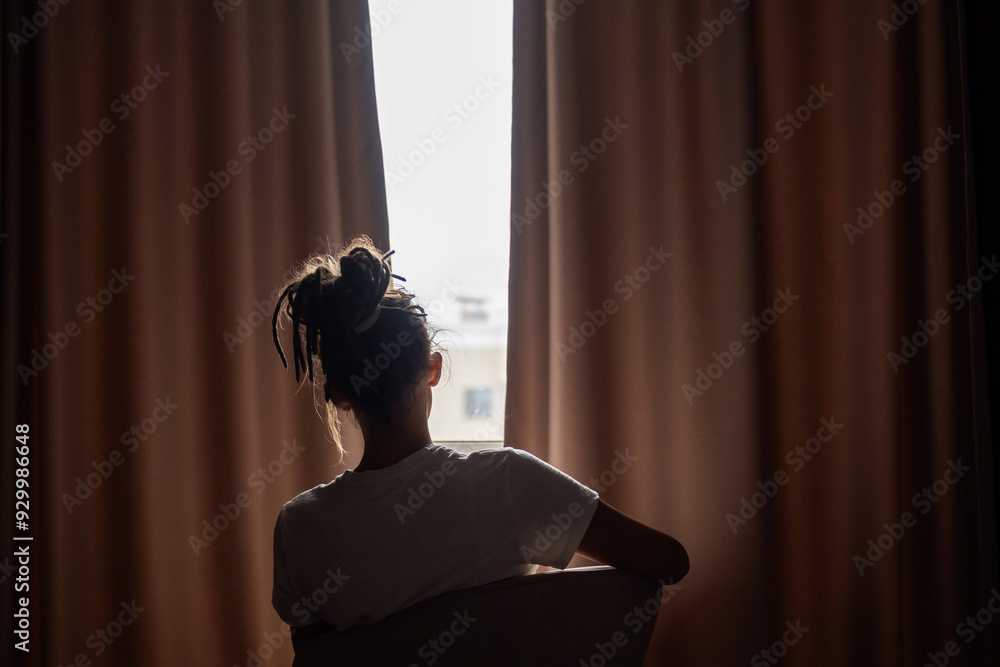 Person silhouetted sitting against light while peering through curtains. Person silhouetted sitting against light while peering through curtains.