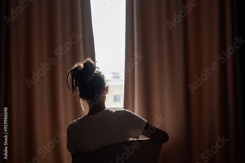 Cuadro en lienzo Person silhouetted sitting against light while peering through curtains