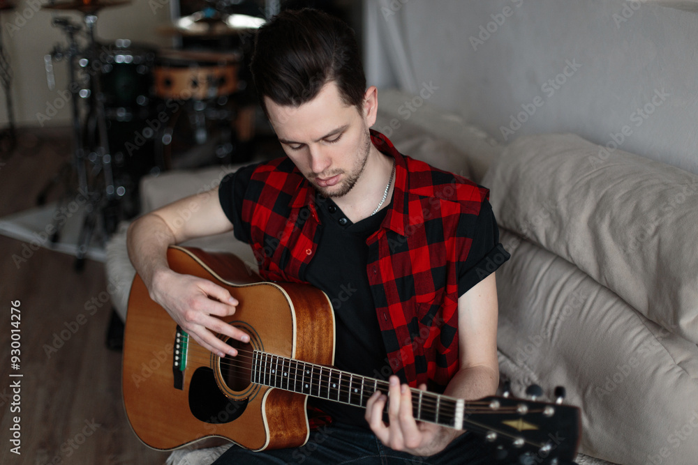 Obraz premium A man sits on a sofa and practices playing the guitar. Music and Hobbies