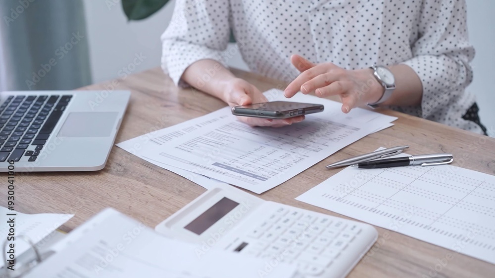 Fototapeta premium Close-up of an adult's hands with smartphone, calculator, and documents on a desk in office. Bookkeeping, finance, audit and taxes. Business concept