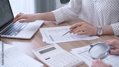 Female bookkeeper or auditor is working on finances papers with a colleague, using magnificent glass, calculator and laptop. Audit and taxes