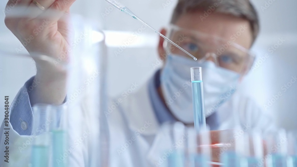 Man with safety glasses and blue mask is working with lab tubes using a pipette in a modern laboratory, close-up of researcher. Science and medicine Man with safety glasses and blue mask is working with lab tubes using a pipette in a modern laboratory, close-up of researcher. Science and medicine