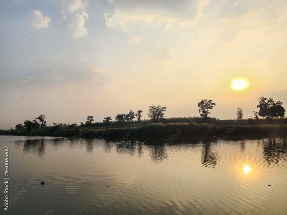 Stock photo of The beautiful sunset view at the lake, surrounded by lush green trees and vast farmland, with the trees reflection floating on waters surface, creating breathtakingly beautiful scenery Stock photo of The beautiful sunset view at the lake, surrounded by lush green trees and vast farmland, with the trees reflection floating on waters surface, creating breathtakingly beautiful scenery