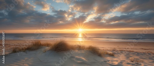  The sun sets over a beach, foreground featuring sand dunes and grass, distant horizon holds a body of water