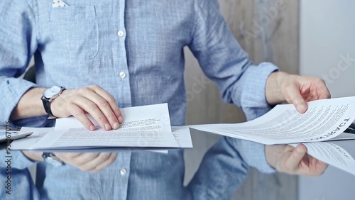 Businessperson analyzing document at desk. Close-up of a professional auditor or lawyer reviewing a lengthy paper report in office setting. Business people concept