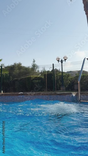 A young girl jumps into a pool, splashing water around, under a clear blue sky, capturing the fun and excitement of summer