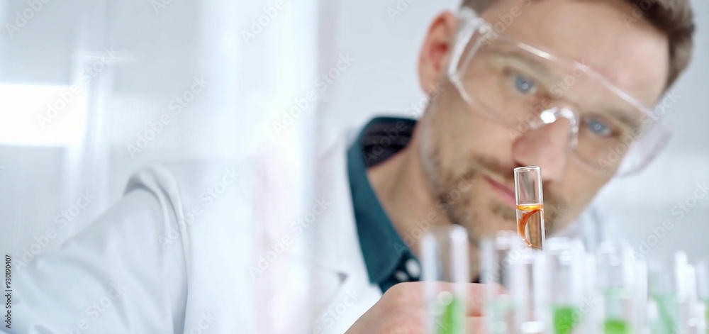 Man researcher with safety glasses is examining lab tube with a orange fluid in a modern laboratory, close-up. Science, microbiology and medicine Man researcher with safety glasses is examining lab tube with a orange fluid in a modern laboratory, close-up. Science, microbiology and medicine