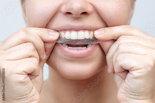 Foto Cropped shot of a young caucasian smiling woman holding a 3d transparent teeth whitening strip to get rid of the dark yellow plaque on a white background