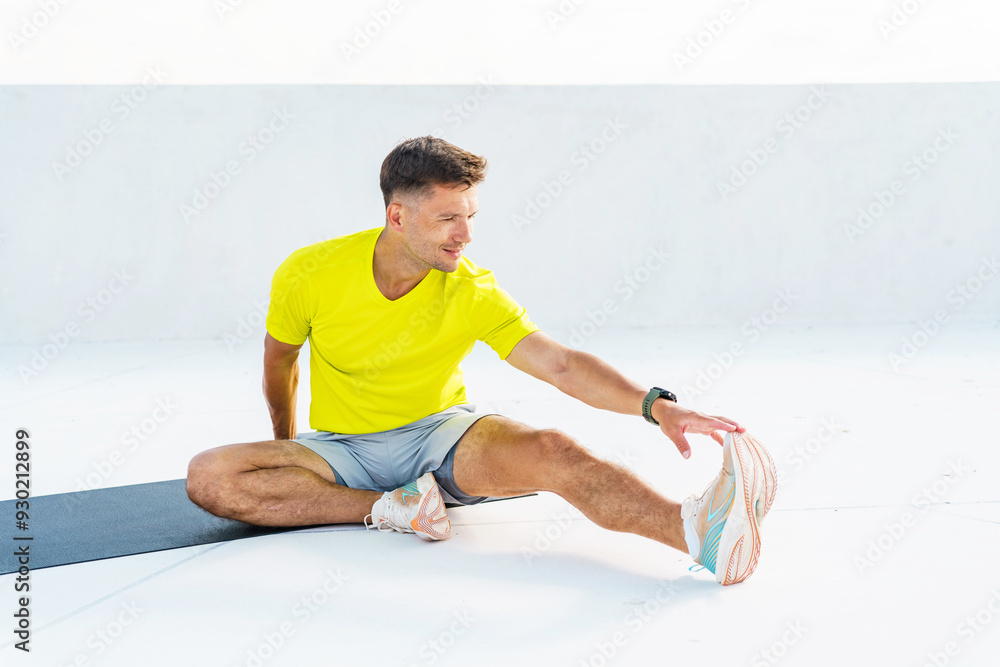 A man in a bright yellow shirt stretches his leg on a mat during an outdoor workout, focused on flexibility and fitness. A man in a bright yellow shirt stretches his leg on a mat during an outdoor workout, focused on flexibility and fitness.