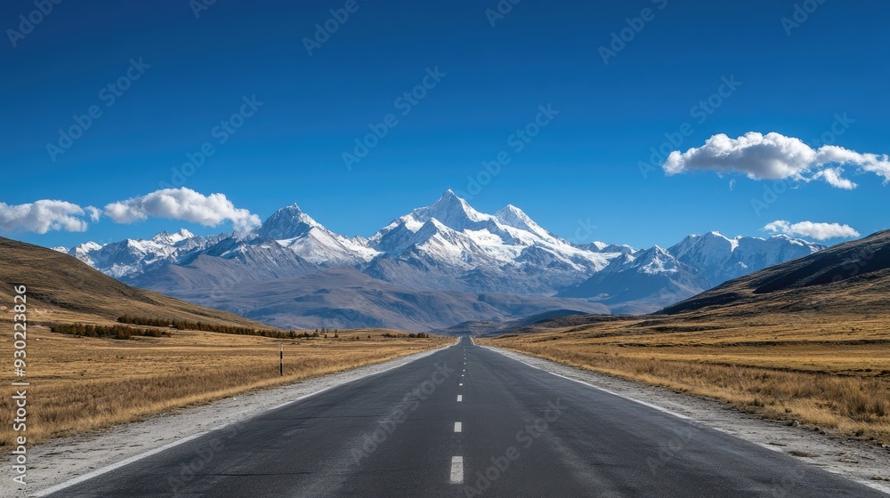 Fototapeta premium A scenic route through a mountainous region, with snow-capped peaks and a clear blue sky.
