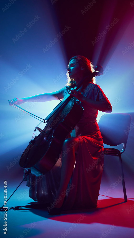 Fototapeta premium Silhouette of beautiful woman, musician playing cello solo on stage in dramatic spotlights and smoke. Stringed instruments. Concept of classical and modern music, entertainment, jazz. Ad