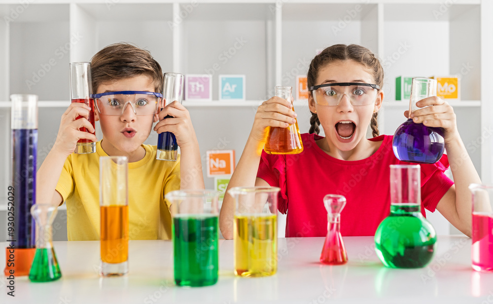 Two enthusiastic children conducting a chemistry experiment in a classroom setting, holding colorful liquids and wearing safety goggles. Two enthusiastic children conducting a chemistry experiment in a classroom setting, holding colorful liquids and wearing safety goggles.