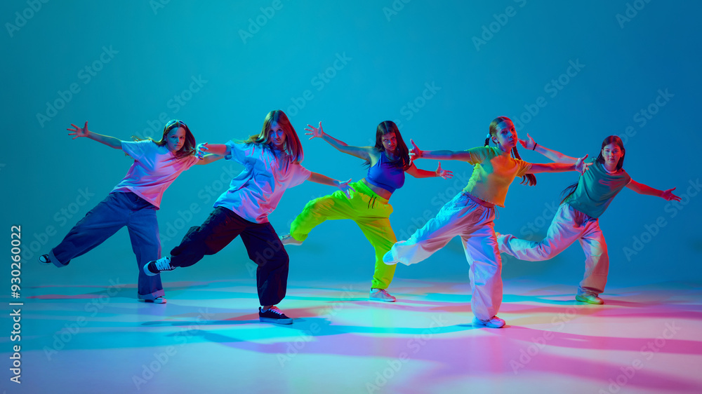 Obraz premium Self-expression through dynamic dance. Young girls, teens performing hip hop on stage against cyan blue background in neon background. Concept of modern dance styles, youth culture, active lifestyle