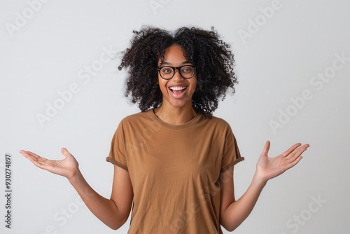 Excited Black woman with curly hair and glasses, brown t-shirt, hands open, white background.