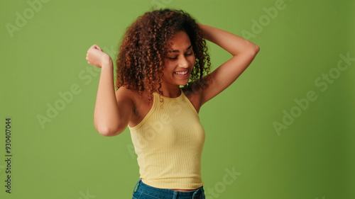 Ecstatic overjoyed African American woman dances carefree, celebrates victory and success, dressed in casual top, feels lively and energetic, isolated on green background photo