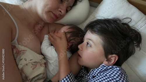 Mother holding newborn baby with young son beside her, tender family bonding, morning routine, cozy home atmosphere, maternal love and care, peaceful and intimate moment, nurturing touch