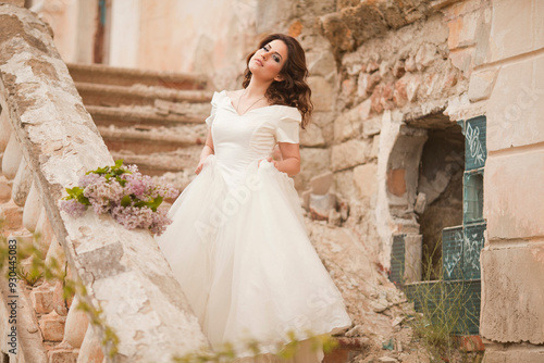 THE EUROPEAN BEAUTIFUL BRIDE WITH THE BEAUTIFUL DARK HAIR WITH THE BOUQUET ON THE BACKGROUND OF THE GREAT BRUSH OF LILAC