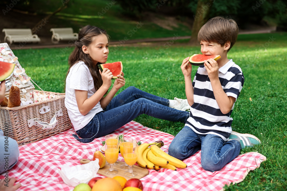 Family picnic. Brother and sister eating watermelon on green grass outdoors Family picnic. Brother and sister eating watermelon on green grass outdoors