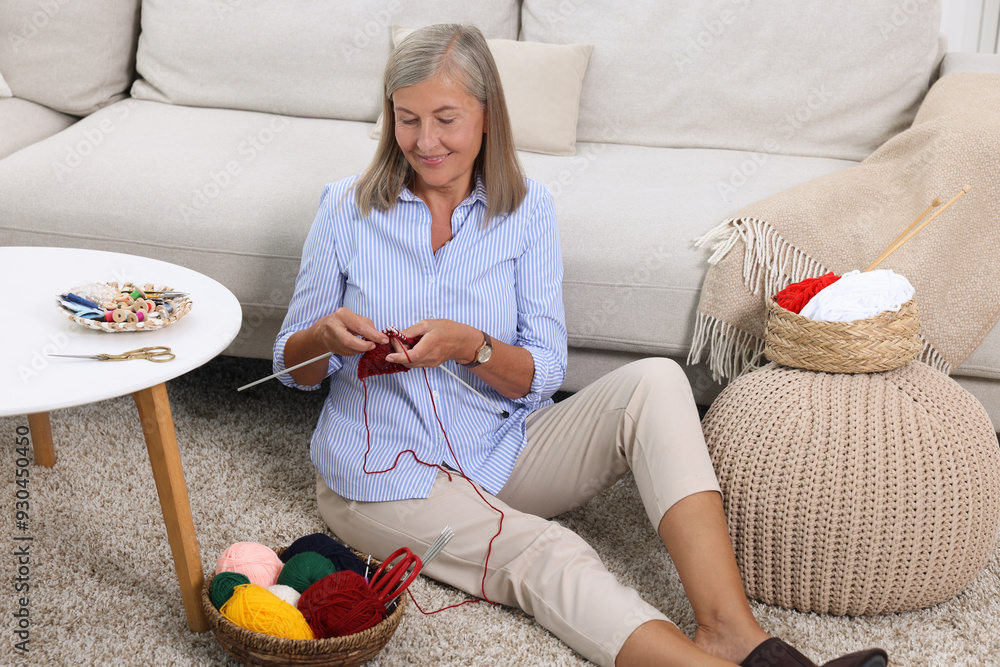 © New Africa - Smiling senior woman knitting near sofa at home