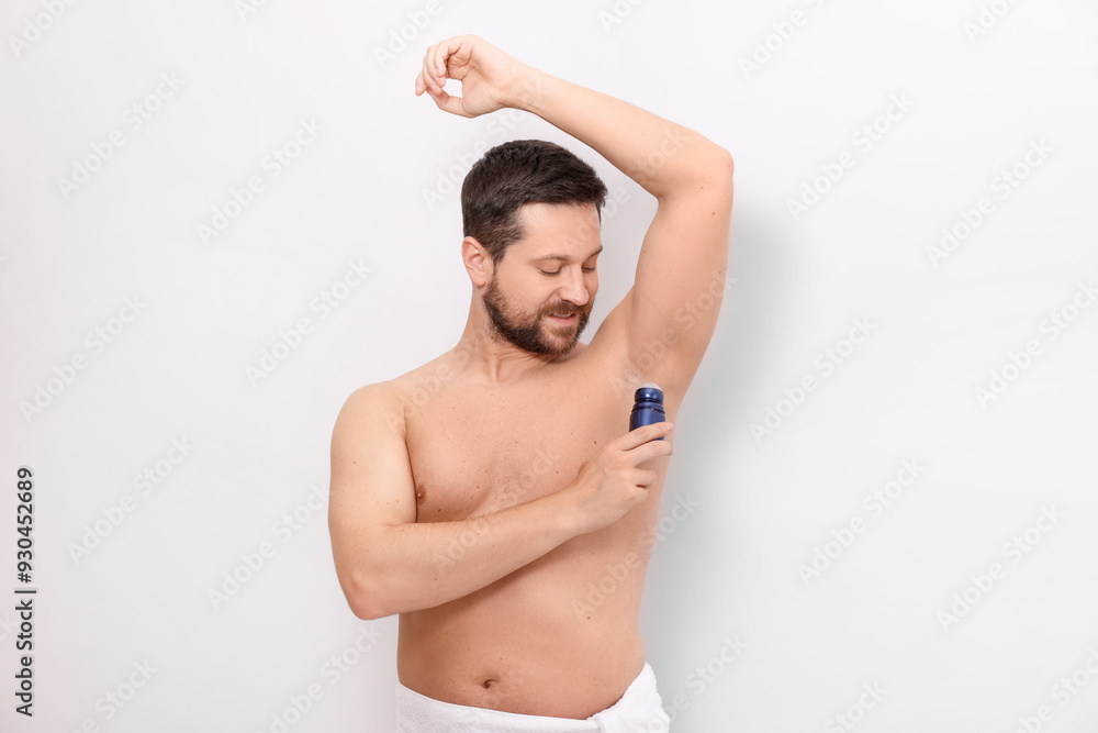 Obraz premium Man applying roll-on deodorant on white background