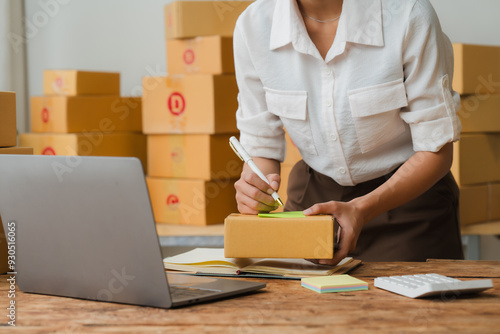 Small Business Owner: A young woman, wearing a white shirt and brown apron, works diligently at a desk surrounded by cardboard boxes, writing a shipping label on a package. Her dedication and hard wor