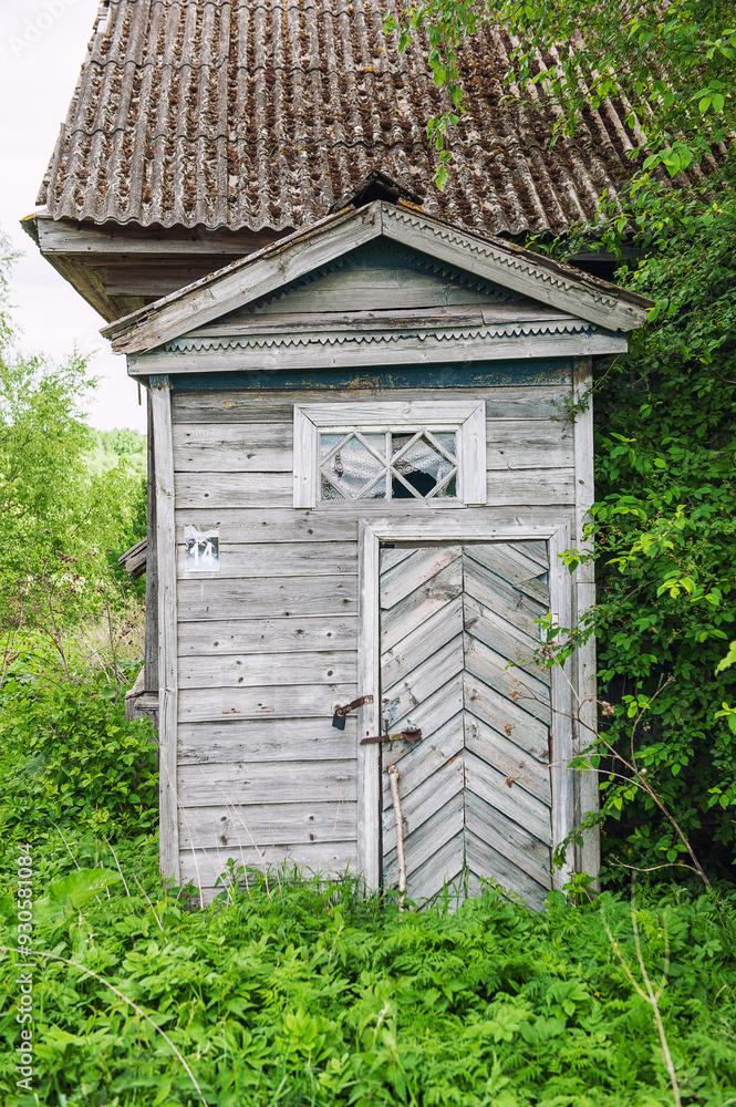 Weathered wooden house with broken window slats sits abandoned, surrounded by overgrown grass Weathered wooden house with broken window slats sits abandoned, surrounded by overgrown grass