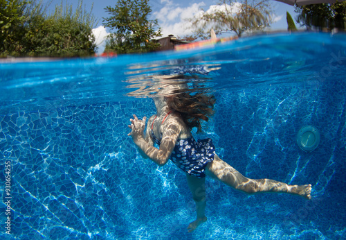 A sporty little girl in a nice swimsuit swims underwater in the pool at the bottom. Underwater photography.