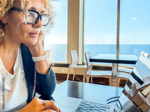 Professional woman working on a laptop at a table aboard a ship while traveling. Captures the essence of digital nomadism and remote work with a stunning sea view and modern connectivity photo