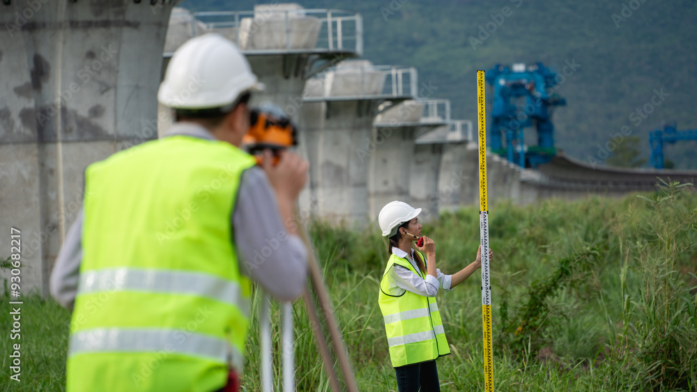 Two Construction workers are standing in a field, one of them holding a yellow tape measure Two Construction workers are standing in a field, one of them holding a yellow tape measure