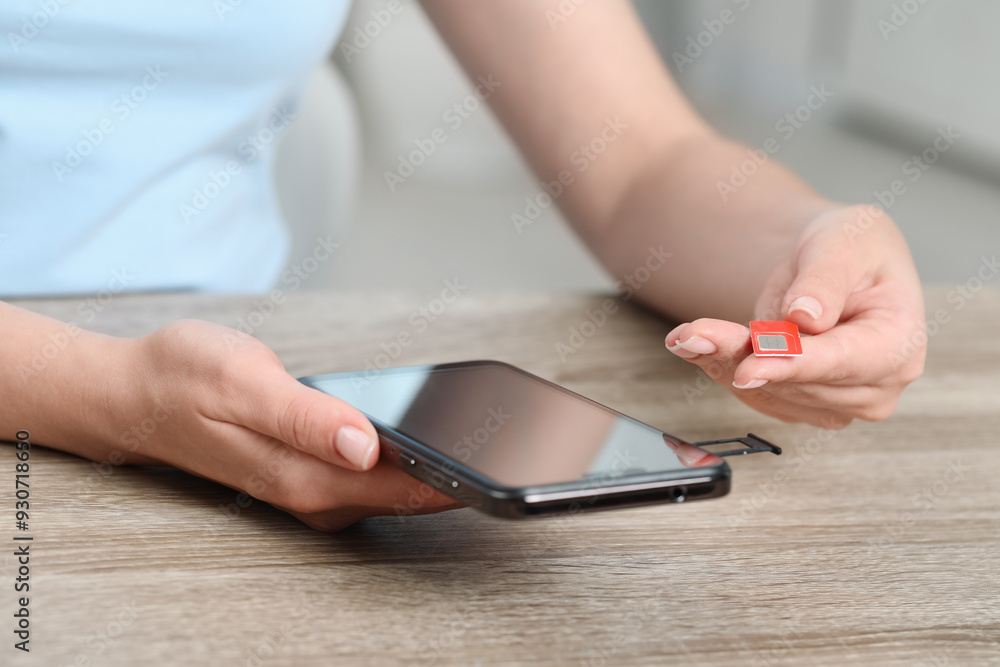 Fototapeta premium Woman holding SIM card and smartphone at wooden table indoors, closeup