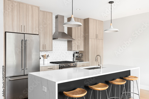 A beautiful, modern kitchen with a dark grey island with a white marble waterfall granite island, wood cabinets, tiled backsplash, and stainless steel appliances. No brands or labels.