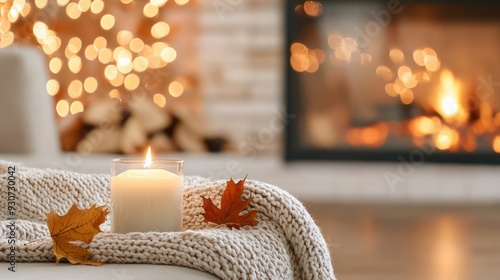 A candle is lit in a glass jar on a blanket next to a fireplace. The scene is cozy and warm, with the flickering candlelight adding to the ambiance