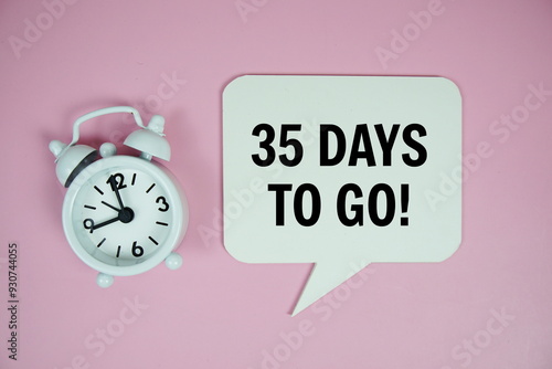 35 Days to go text on speech bluble with alarm clock top view on pink background photo