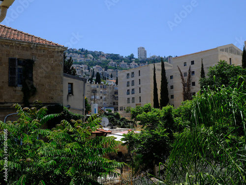 Verdant cityscape of Haifa, Israel showcasing ancient and modern buildings under a clear blue sky, nestled on a lush hillside. photo