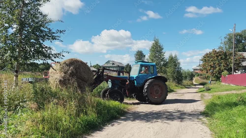A scenic rural landscape shows a blue tractor on a dusty path winding through A scenic rural landscape shows a blue tractor on a dusty path winding through