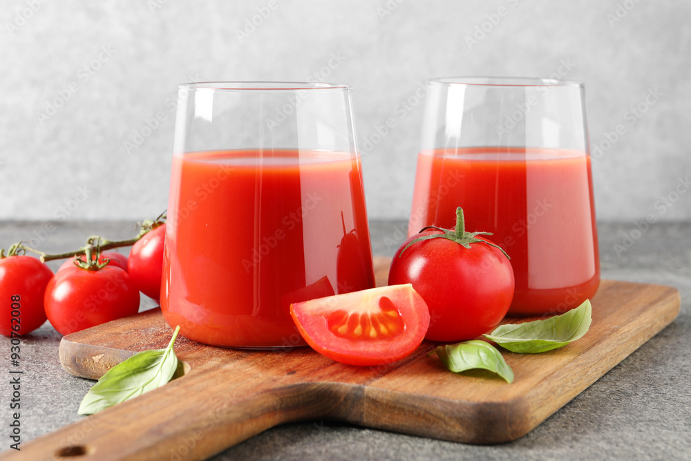 Tasty tomato juice in glasses, basil and fresh vegetables on grey table Tasty tomato juice in glasses, basil and fresh vegetables on grey table