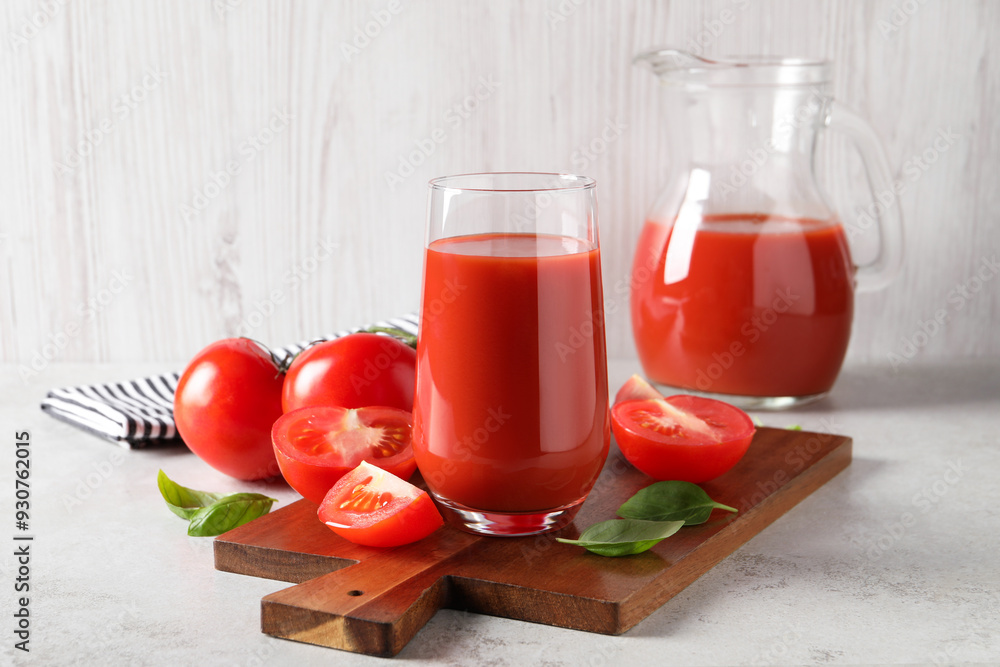 Tasty tomato juice in glass, basil leaves and fresh vegetables on light grey table Tasty tomato juice in glass, basil leaves and fresh vegetables on light grey table