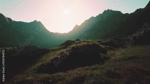 The sun shines brightly over a rugged mountain range, illuminating the peaks and valleys below.
