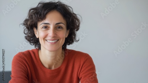 A woman with curly hair is smiling and wearing an orange sweater